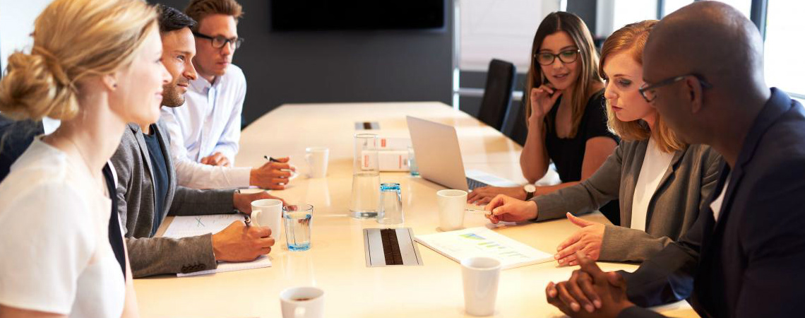 A mixed group of young professionals gather to collaborate around a conference table.