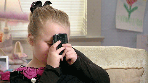 A young girl presses a smartphone to her forehead.