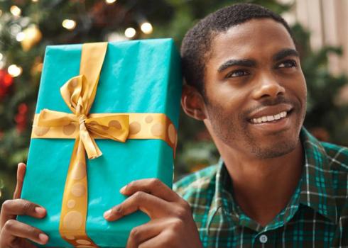 A young man shakes a wrapped present, listening to guess what's inside.