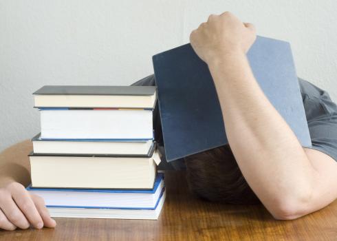 Beside a stack of books, an overwhelmed student hides his head...and maybe catches 40 winks.