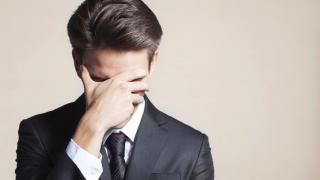 A young man in a business suit covers his face with his hand in shame