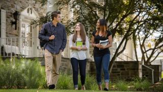 Three college students walk across the quad, away from an academic building.