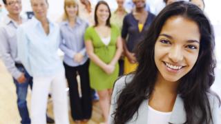 Ready for their team selfie, a group of people gather behind a young woman in business attire.