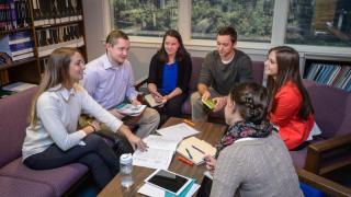 Gathered around a small table in the library, a group of college students study together.