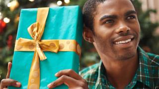 A young man shakes a wrapped present, listening to guess what's inside.