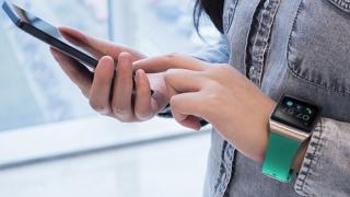 A woman wearing an Apple watch taps the smartphone in her other hand