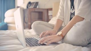 Woman working on a laptop on her bed.