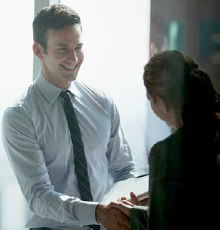 A young man shakes hands with a woman in a business setting.